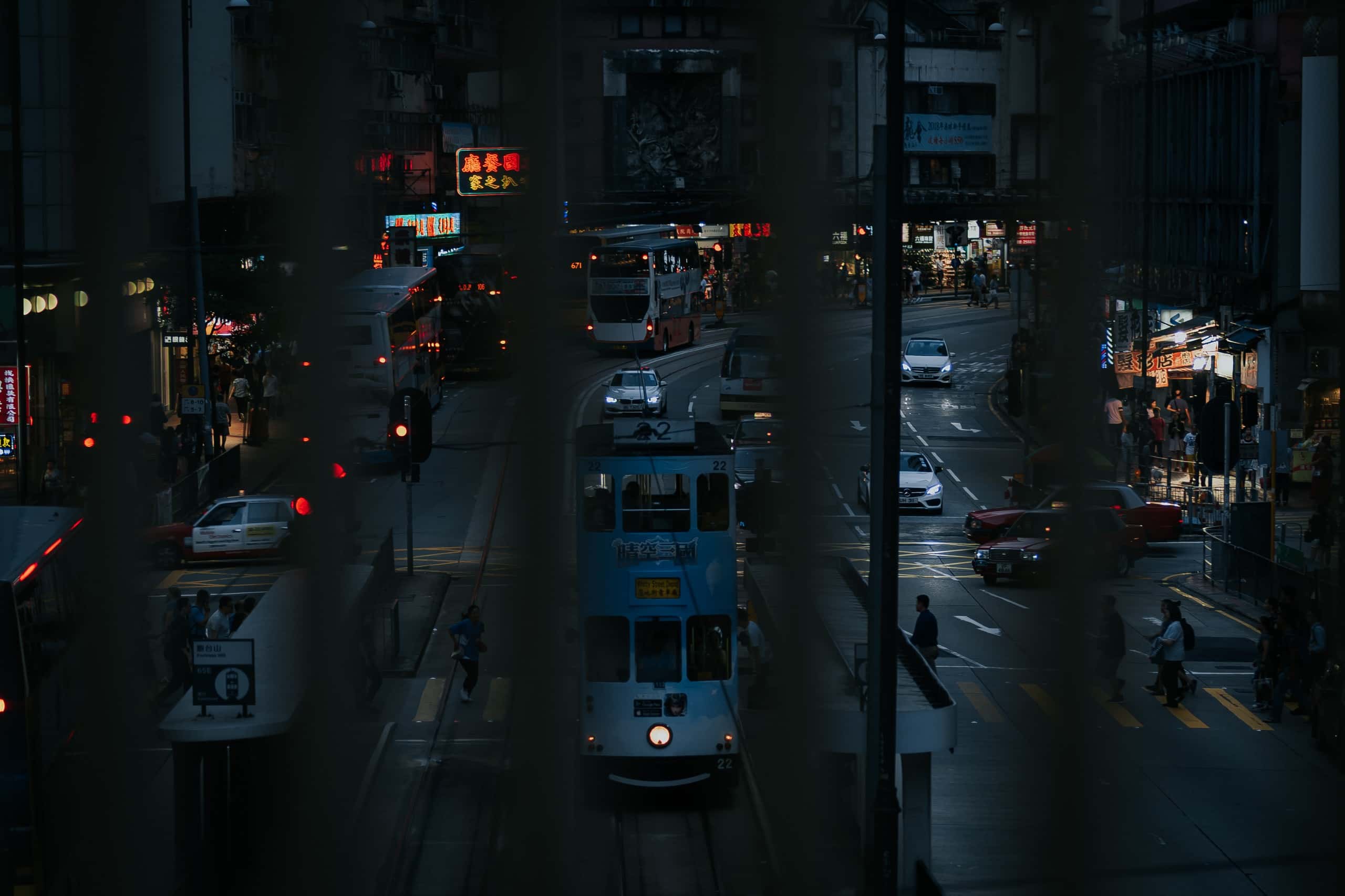 入夜後的香港街道，電車緩緩駛過，霓虹招牌下人車往來。