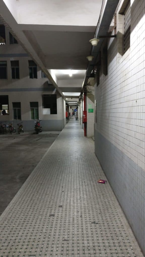 宿舍或工廠建築的長走廊，地面鋪有階磚，一旁停放著單車與電單車