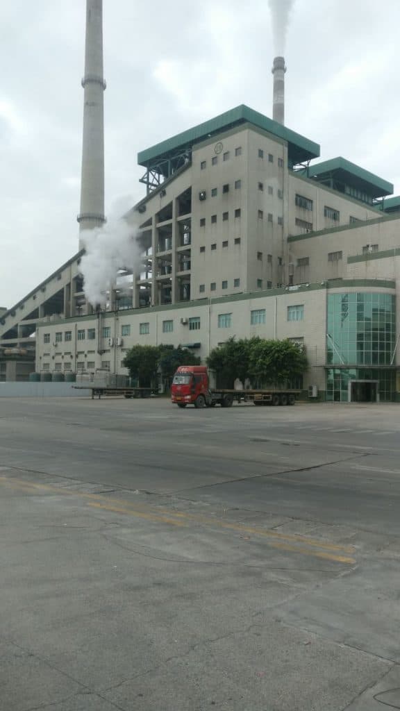 工廠外貌：煙囪冒出白煙，廠房前的空地上停著一輛紅色貨櫃車
