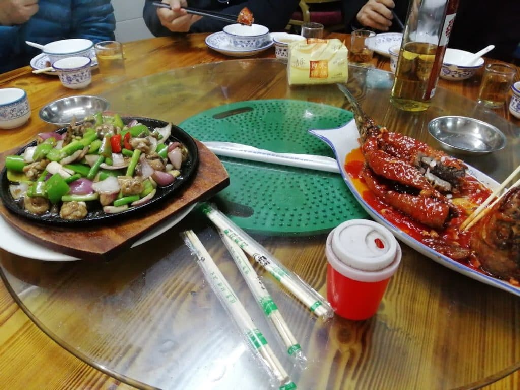 圓桌上的中式菜餚：鐵板炒菜與淋上紅醬的燒魚，桌上放有筷子、茶杯與紙巾