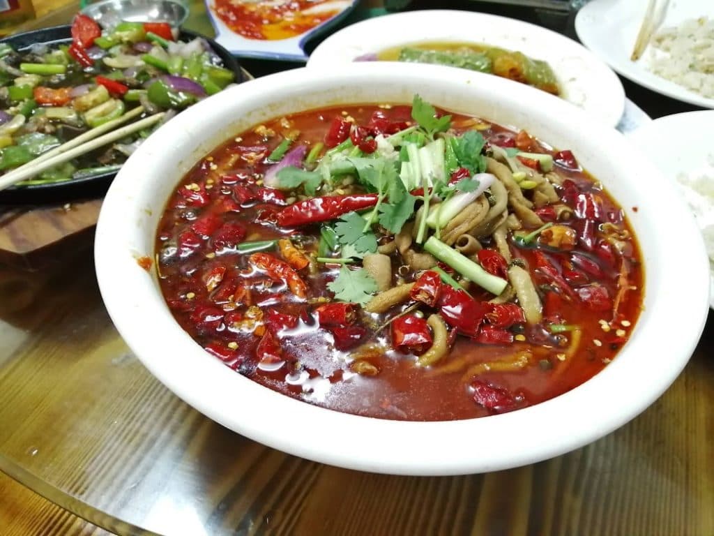 一大碗四川風味紅油辣菜，鋪滿乾辣椒與芫荽，旁邊還有其他菜式