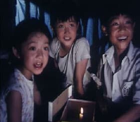 舊電影截圖：三名兒童圍在燭光旁，神情驚訝地望向鏡頭