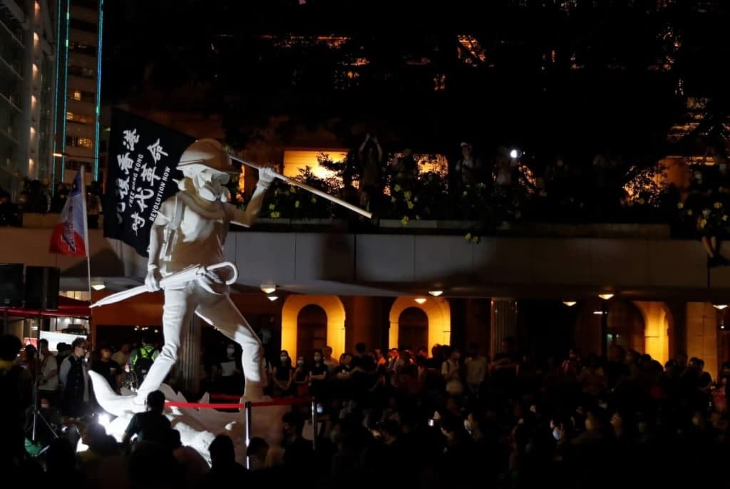 夜間集會中，一座手持旗幟的白色人像雕塑矗立在人群中央