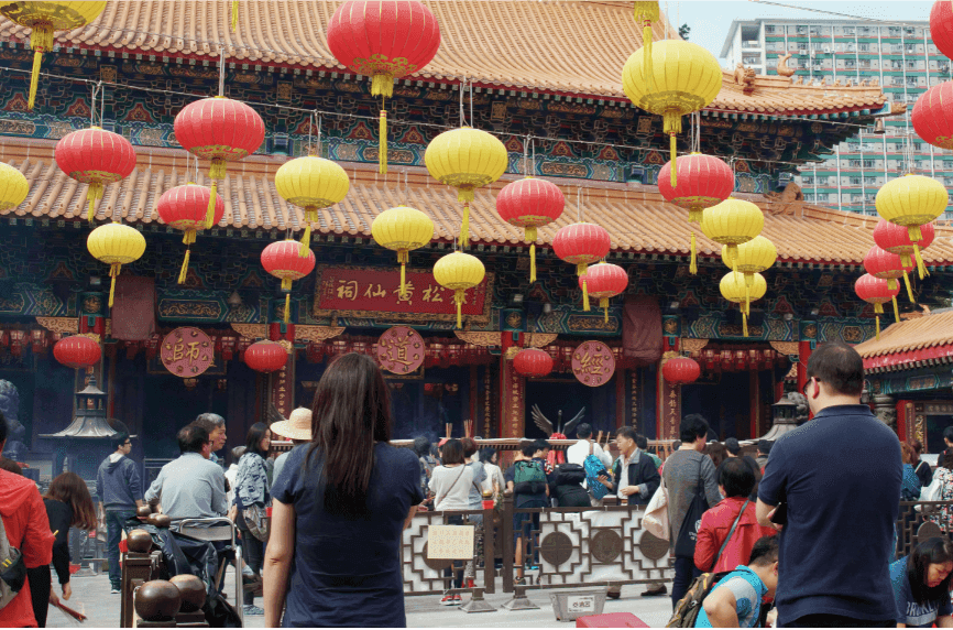 香港黃大仙祠正殿前,紅黃燈籠高掛,善信在殿前上香參拜