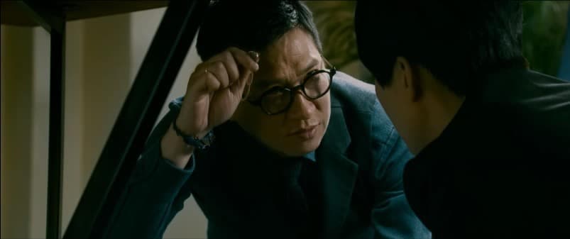 電影劇照:一名戴眼鏡的男子手扶鏡框,凝視前方的另一名男子
