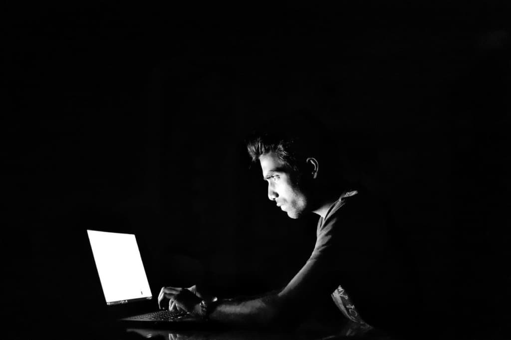 黑白照片:一名男子在漆黑房間中對著發光的手提電腦螢幕打字