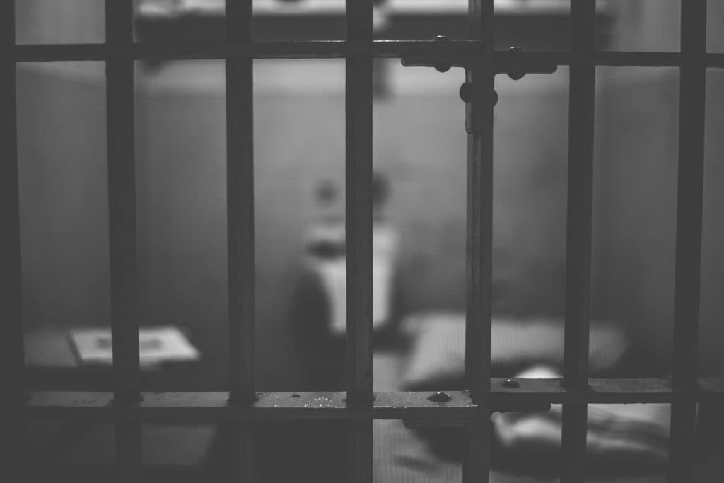 黑白照片:透過監倉鐵欄望向倉內,床鋪與物件在後方虛化